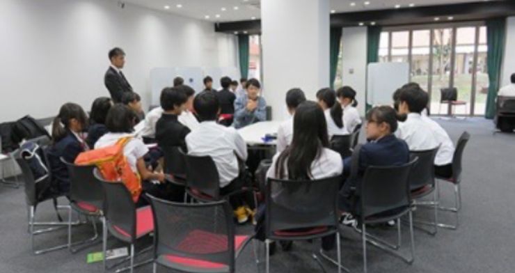写真：複数の大きなテーブル席で学生が高校生に話をしている